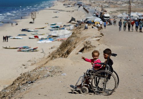 Displaced Palestinian children sit in a wheelchair by the side of a road, after Hamas agreed to release hostages and accept some other terms in a U.S. plan to end the war, in the central Gaza Strip, October 4, 2025. REUTERS/Mahmoud Issa