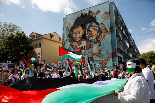 Activists hold a Palestinian flag in front of a mural during a protest march