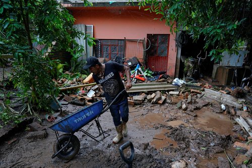 A man uses a wheelbarrow to remove mud and debris from a home as torrential rains from tropical storm Raymond