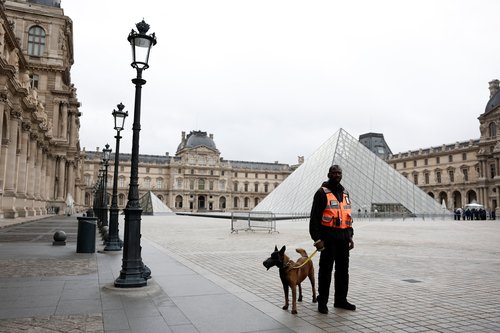 A security employee with a dog stands near the glass Pyramid of the Louvre Museum