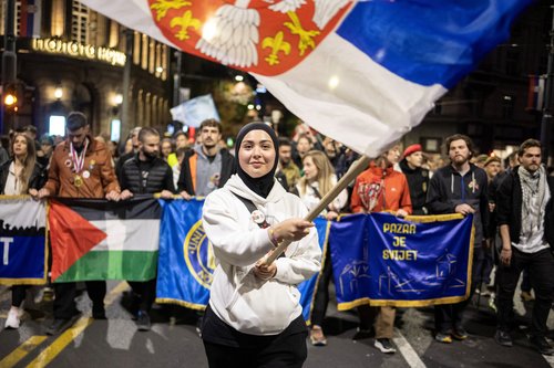 A woman waves a flag while students from Novi Pazar light