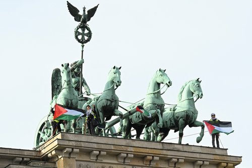 Pro-Palestinian protesters present flags of Palestine after unveiling a banner reading, “Never again genocide - Freedom for Palestine”, on top of Brandenburg Gate in Berlin, Germany, November 13, 2025. REUTERS/Annegret Hilse