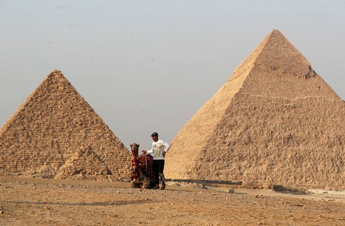 A man with his camel waits for tourists in front of the Great Pyramids of Giza