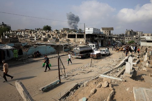 Palestinians walk past damaged graves as smoke rises following an Israeli strike, in Gaza City, August 13, 2025. REUTERS/Dawoud Abu Alkas REFILE - QUALITY REPEAT TPX IMAGES OF THE DAY