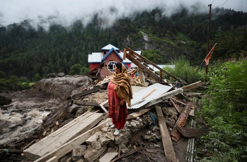 A woman stands in front of houses damaged by the deadly flood caused by sudden, heavy rain in Chasoti town of Kishtwar district, Indian Kashmir, August 15, 2025. REUTERS/Stringer