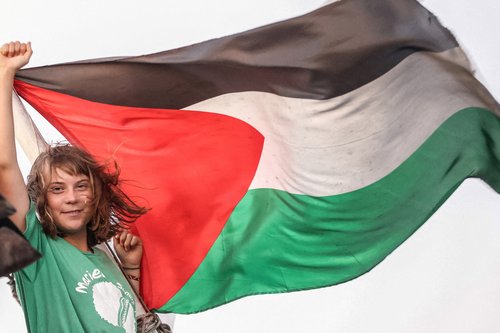 Greta Thunberg gestures next to a Palestinian flag on a ship