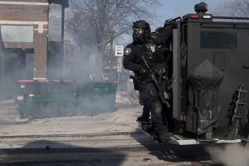 A Minneapolis Police Department officer rides on the back of a vehicle, during clashes with community members at the scene where federal agents fatally shot a man while trying to detain him, in Minneapolis, Minnesota, U.S., January 24, 2026. REUTERS/Tim E