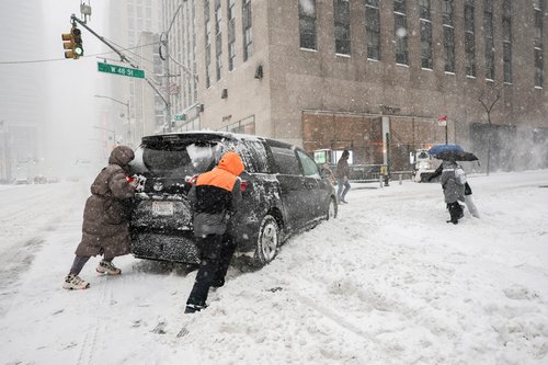 People help by pushing a vehicle near Times Square as a major winter