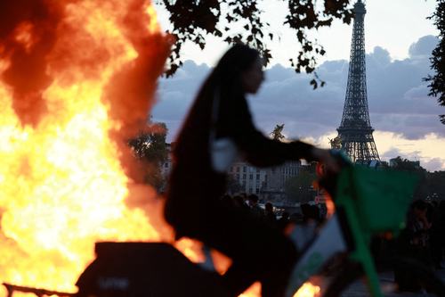 FILE PHOTO: A woman rides a bicycle past a burning barricade near the