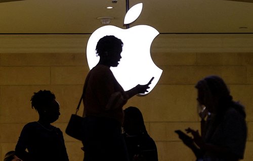 FILE PHOTO: A woman uses her iPhone mobile device as she passes a lighted Apple logo at the Apple store in New York