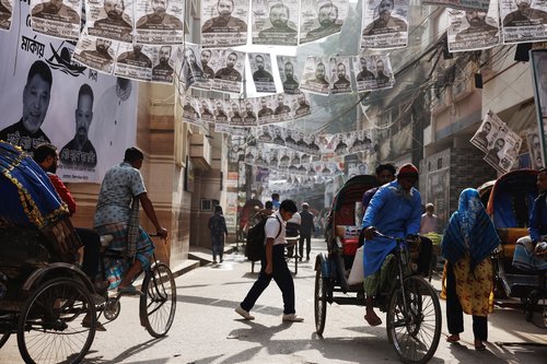 Commuters pass by as posters of an election candidate hang on the street ahead of general election in Dhaka