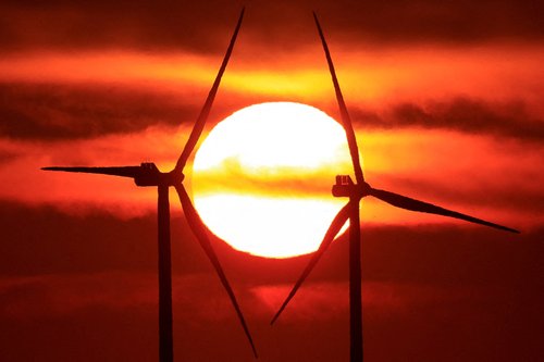 FILE PHOTO: Power-generating windmill turbines and electricity pylons are pictured during sunrise at a wind park in Avesnes-le-Sec