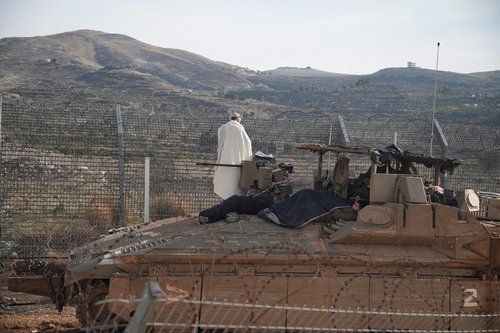 Israeli soldiers on a Namer Armoured Personnel Carrier (APC) while one of them conducts morning prayers, along the Golan Heights side of the ceasefire line between Syria and the Israeli-occupied Golan Heights