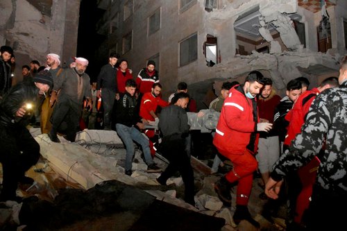 Rescuers carry a person on a stretcher at the site of a collapsed building, following an earthquake, in Hama