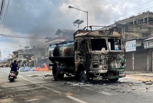 A scooterist rides past a damaged water tanker that was set afire during a protest by tribal groups in Churachandpur
