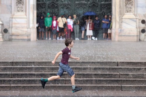 Tourists take shelter under the Duomo Cathedral as heavy rain hits Milan