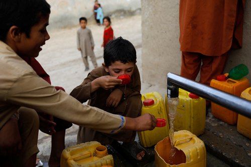 An Afghan boy drinks water as he and others fill their containers from a tap in Nahr-e-Shahi district in Balkh province