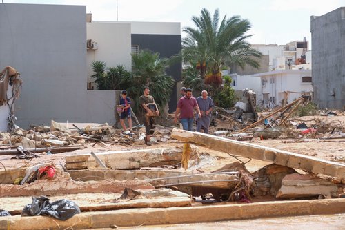 People walk between the debris, after a powerful storm and heavy rainfall hit Libya, in Derna