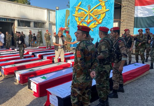 Military police stand near coffins with the bodies of some of the people who were killed in a drone attack on a military academy, outside a military hospital in Homs