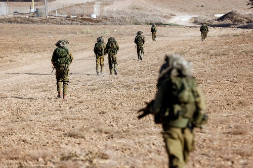 Israeli soldiers walk on grassy terrain near Israel's border with Gaza in southern Israel