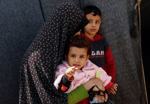 A displaced Palestinian woman sits with children, amid the ongoing conflict between Israel and Palestinian Islamist group Hamas, in a tent camp in Khan Younis in the southern Gaza Strip