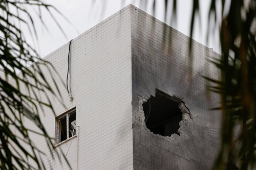 People stand next to a building which was hit by a rocket fired from Gaza, in Ashkelon