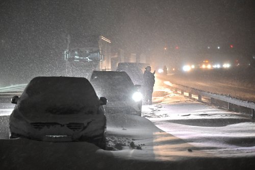 Vehicles wait in line on a snow-covered road following a snowfall in Ekerod
