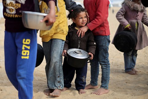 FILE PHOTO: Displaced Palestinian children wait to receive free food at a tent camp, amid food shortages, in Rafah