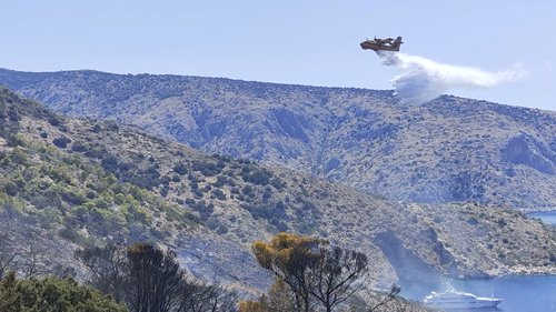 A firefighting plane drops water over an area affected by a forest fire on the island of Hydra