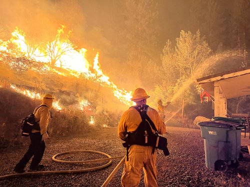 A firefighter uses a hose as vegetation burns on the background, amid the Gold Ranch fire in Verdi