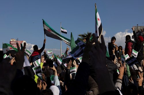 People salute the Syrian opposition flag as its raised on a mast during a gathering after Friday prayers in Latakia