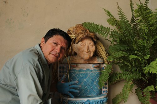 Luis May Ku, 49, poses next to a clay sculptor of an elderly woman from his community of Dzan, wearing a wooden mask adorned with dried palm leaves and painted in Maya Blue taken on 9 September,