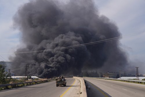 Smoke rises while members of the Syrian forces ride on a vehicle in Latakia