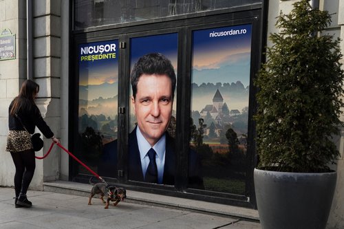 FILE PHOTO: A woman walks a dog past a poster of independent presidential candidate Nicusor Dan