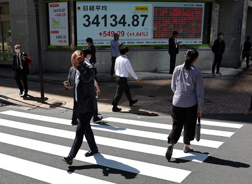 Pedestrians walk past a stock quotation board showing Nikkei share average outside a brokerage in Tokyo