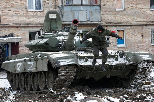 A service member of pro-Russian troops jumps off a tank outside a residential building which was damaged during Ukraine-Russia conflict in Volnovakha