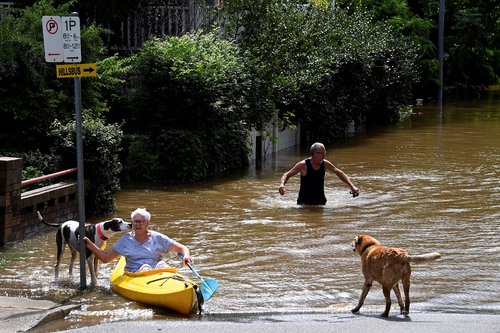 A resident paddles through floodwater as a road is submerged in Windsor, north-west of Sydney