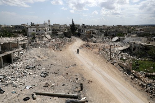 FILE PHOTO: Men ride a motorbike past damaged buildings in the rebel-held town of Nairab