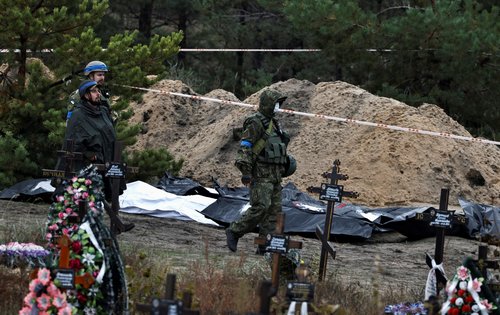Army officers walk past bodies exhumed from, what Ukrainians said, a mass grave, in the newly recaptured town of Lyman