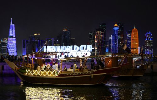 People dance on a traditional boat as they pass by the skyline of Doha