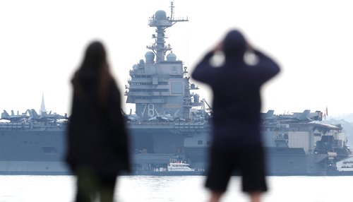 A couple stand on a beach near the USS Gerald R Ford aircraft carrier, currently anchored in the Solent near Gosport