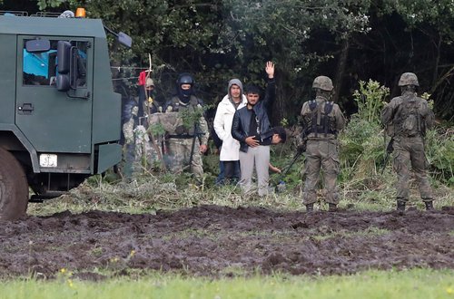 Polish border guard officers stand next to a group of migrants stranded on the border between Belarus and Poland near the village of Usnarz Gorny