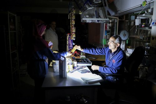 People shop in a grocery store under a portable electric light during a power cut near Bhamdoun