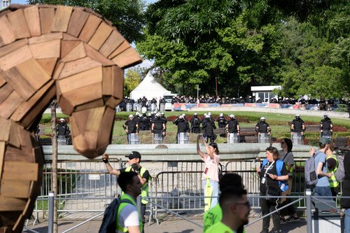 Police in riot gear stand guard as people march next to a mock Trojan horse