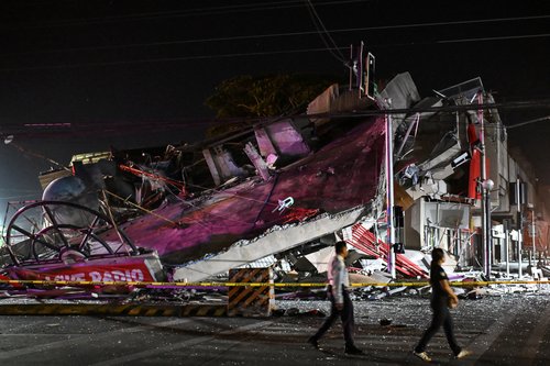People walk past a collapsed building following the magnitude
