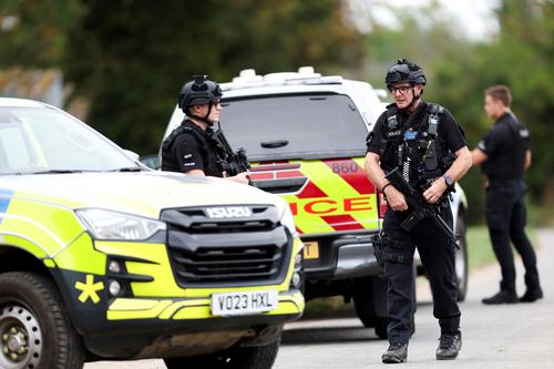 Armed police officers work on a road outside the perimiter of the RAF Fairford airbase, after police declared a major incident at the base after several men were arrested on suspicion of offences under the Explosives Act, in Fairford