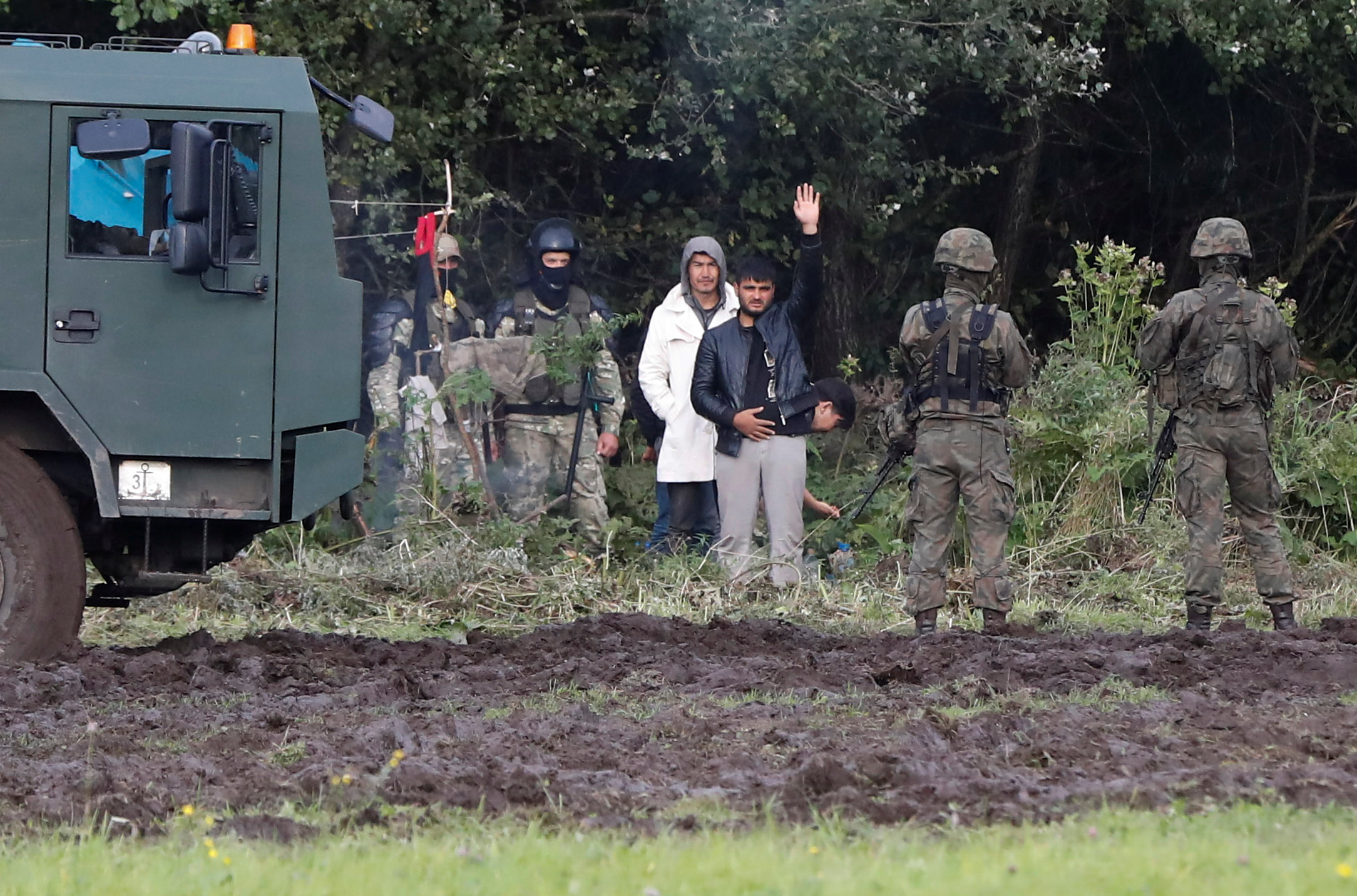 Polish border guard officers stand next to a group of migrants stranded on the border between Belarus and Poland near the village of Usnarz Gorny