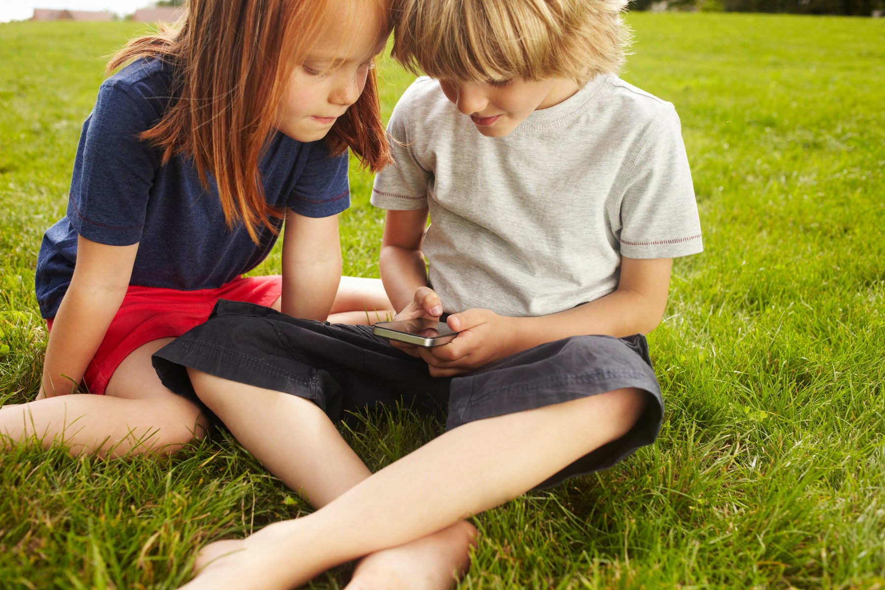 Children using cell phone in grass