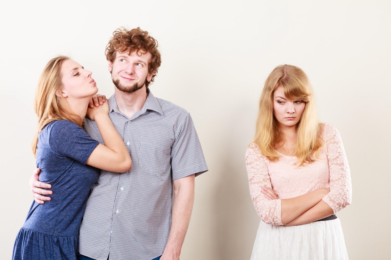 Jealousy and betrayal concept. Abandoned jelous girl watching on happy hugging couple. Triangle relationship.