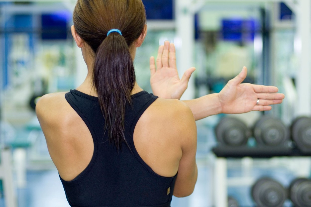 A female fitness instructor demonstrates a shoulder stretch in a gym